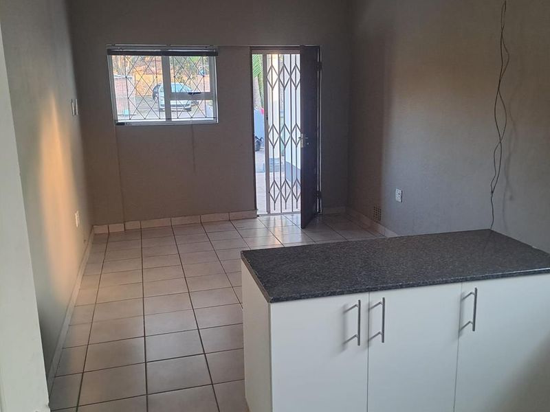 Open-plan living area featuring tiled flooring, a kitchen island with granite countertop, and direct access to the exterior via a security gate.