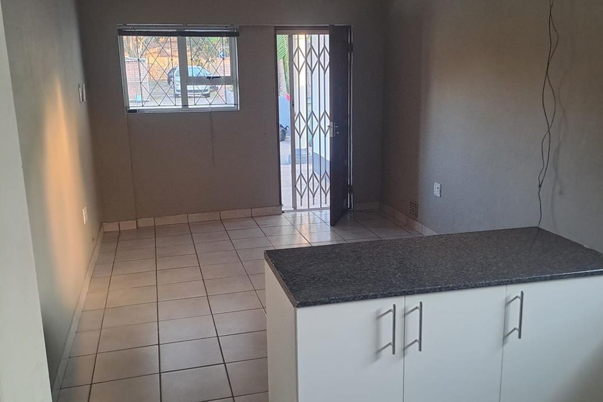 Open-plan living area featuring tiled flooring, a kitchen island with granite countertop, and direct access to the exterior via a security gate.