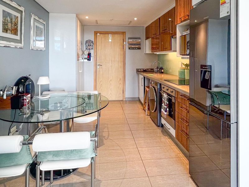 A modern open-plan kitchen and dining area featuring sleek wooden cabinetry, integrated appliances, and polished floor tiles.
