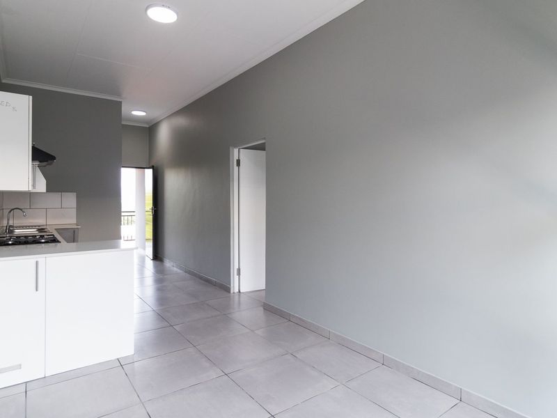 An open-plan living and kitchen area featuring modern grey tiled floors, neutral walls, and a compact kitchen with built-in cabinetry and gas hob.