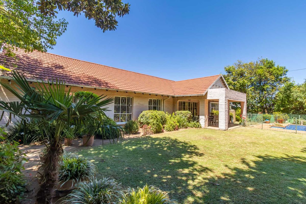Rear view of the property featuring a spacious garden, covered patio area, and a swimming pool with security fencing.