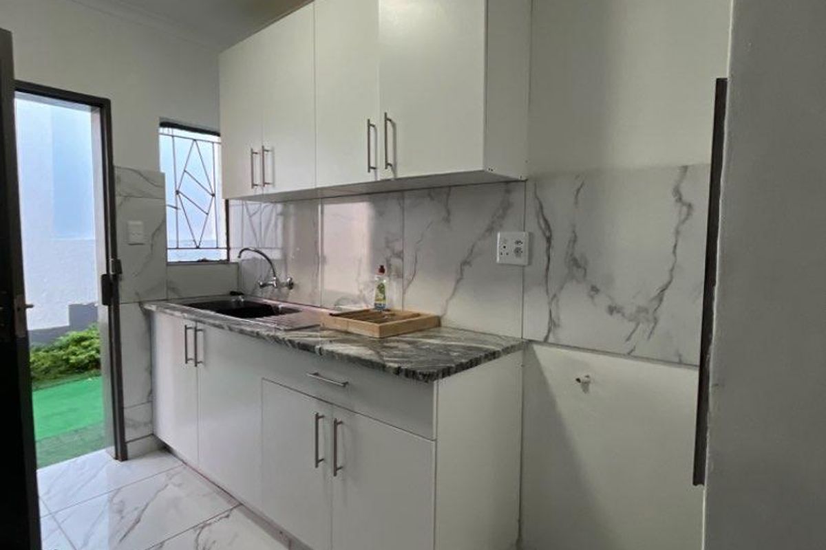 Compact kitchen featuring white cabinetry, marble-look tiled flooring and backsplash, stainless steel sink, and direct access to an outdoor area.