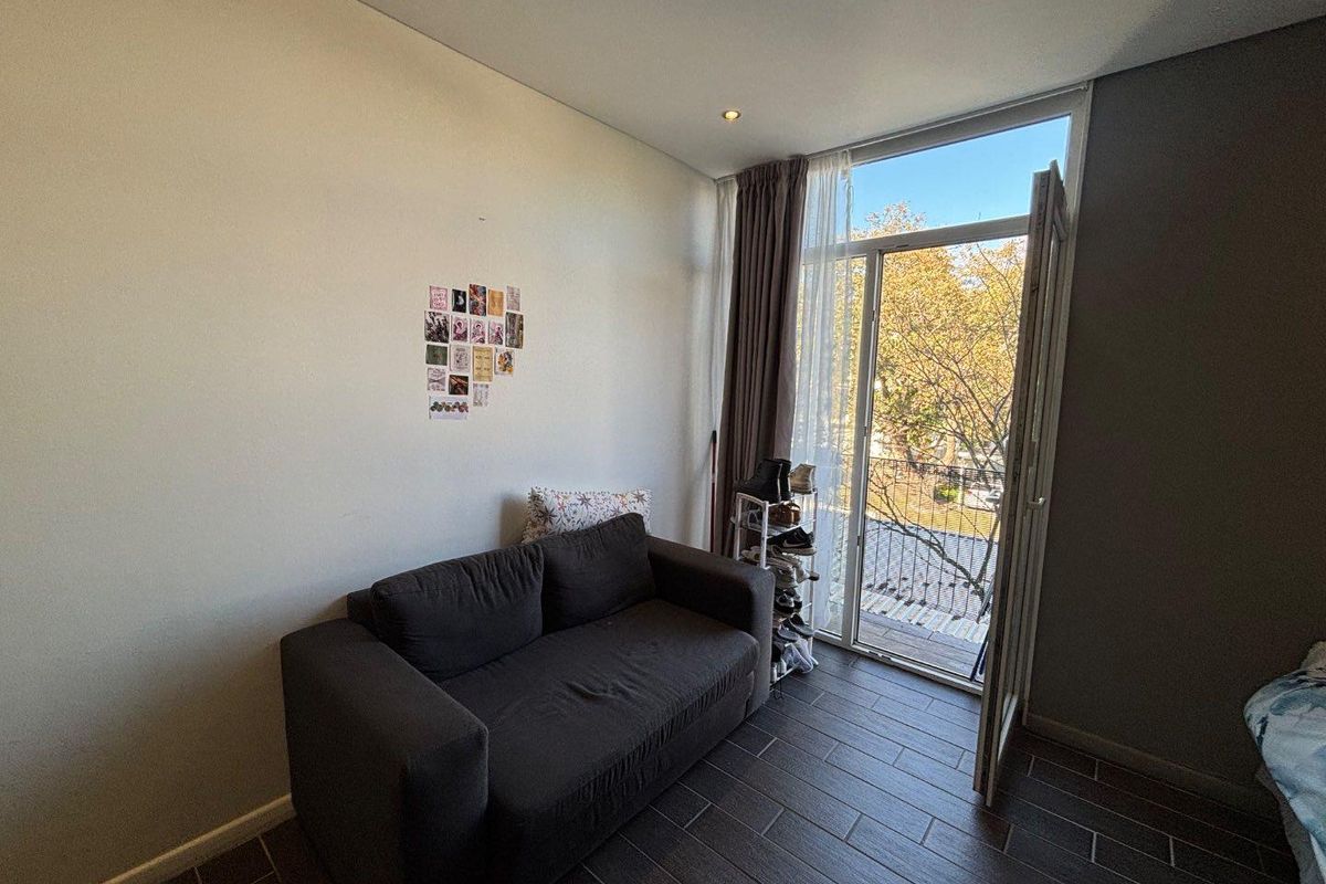 A living area featuring modern tiled flooring and a full-height glass door providing access to an outdoor space with natural light.