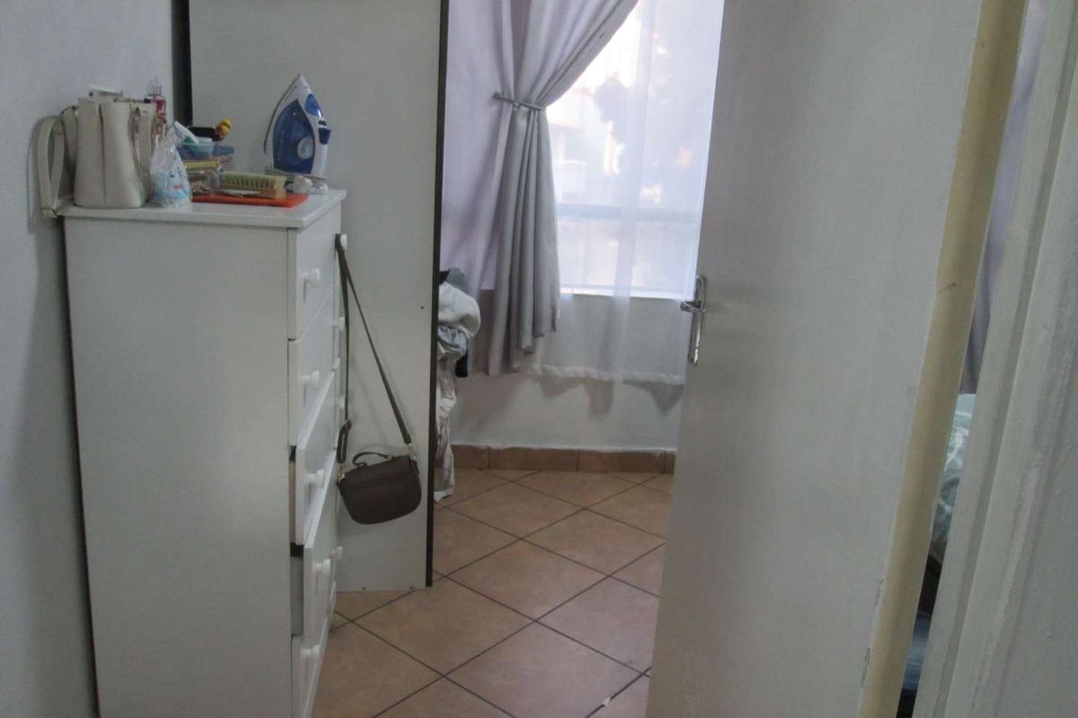 A view into a bedroom featuring tiled flooring and a window with curtains, captured from the doorway.