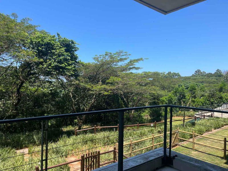 A balcony featuring a metal railing with an elevated view overlooking a lush green garden and surrounding trees.