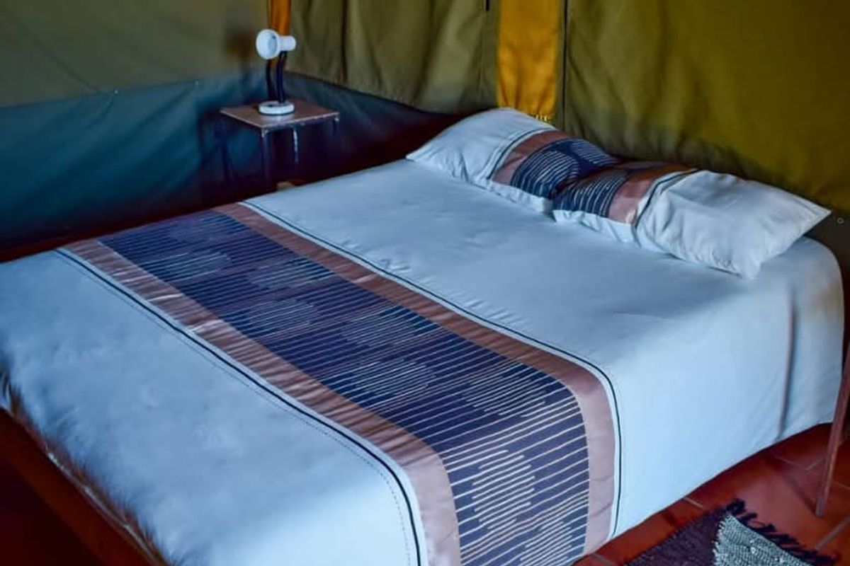 A bedroom within a tented lodge structure featuring canvas walls and tiled flooring.