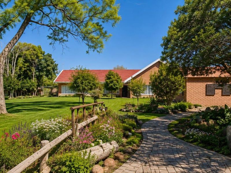 A well-maintained rear garden featuring a paved walkway, mature trees, and a brick-faced home with a tiled roof.