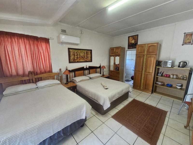 A spacious bedroom featuring tiled flooring, an integrated air conditioning unit, and direct access to an en-suite bathroom.