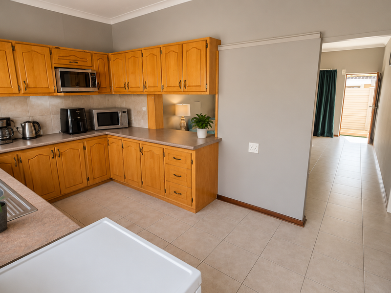 A functional kitchen featuring wooden cabinetry, laminate countertops, tiled backsplash, and ceramic flooring, with an open layout leading to an adjacent hallway.