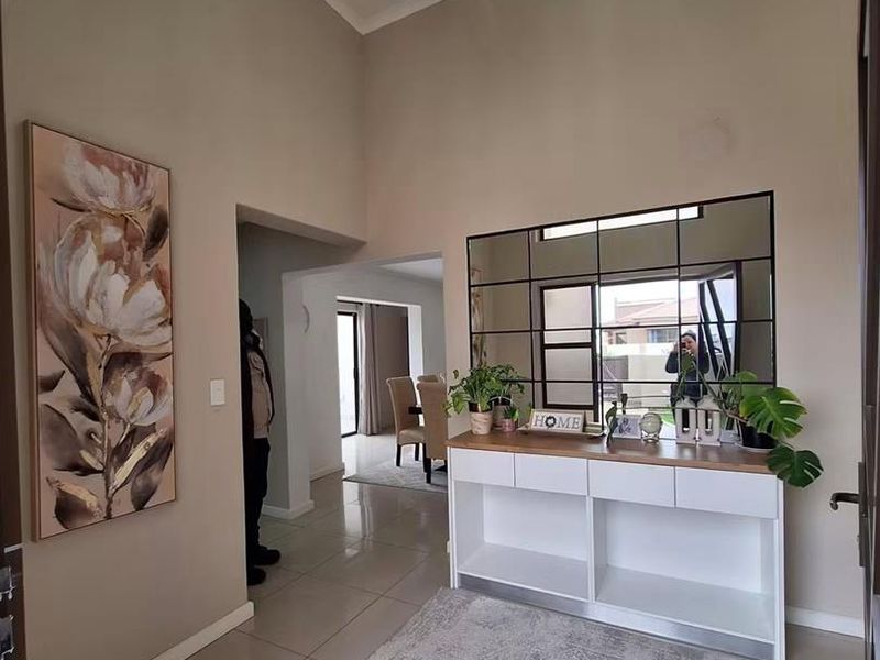 A bright and welcoming entrance hall featuring high vaulted ceilings, a modern crystal chandelier, and sleek tiled flooring leading into the main living area.