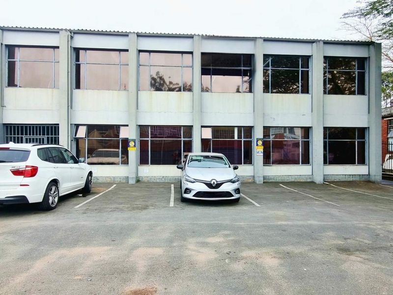 Front elevation of a two-story industrial office building featuring a concrete facade, large windows, and an asphalt parking area.