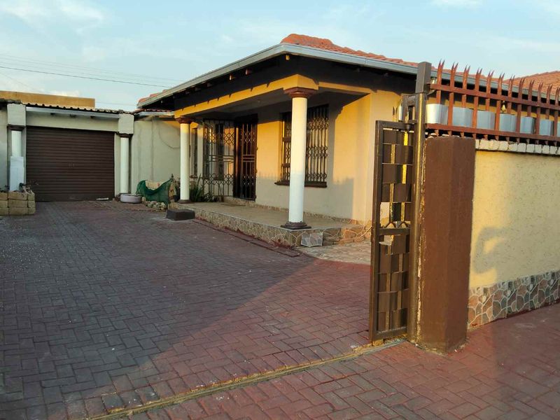 Front exterior view of a house featuring a paved driveway, secure perimeter wall, gated entrance, and a covered porch area.
