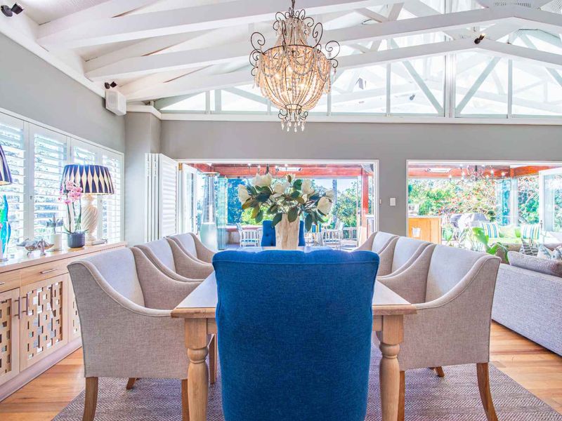 Spacious open-plan living and dining area featuring vaulted ceilings with exposed rafters, timber flooring, and seamless indoor-outdoor flow through large bi-fold doors.