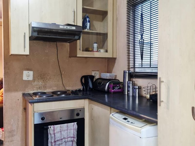 Compact kitchen featuring built-in cabinetry, electric hob, oven, and extractor fan. The space requires cosmetic updates to the walls and ceiling finishes.