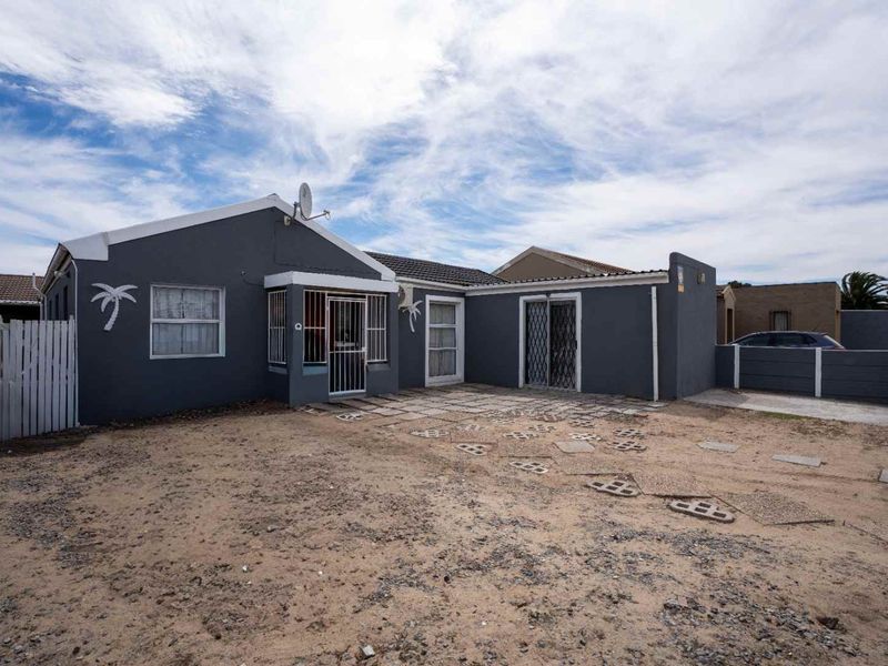 Rear exterior view of the property featuring a paved patio area, security gates, and a large unlandscaped yard space.