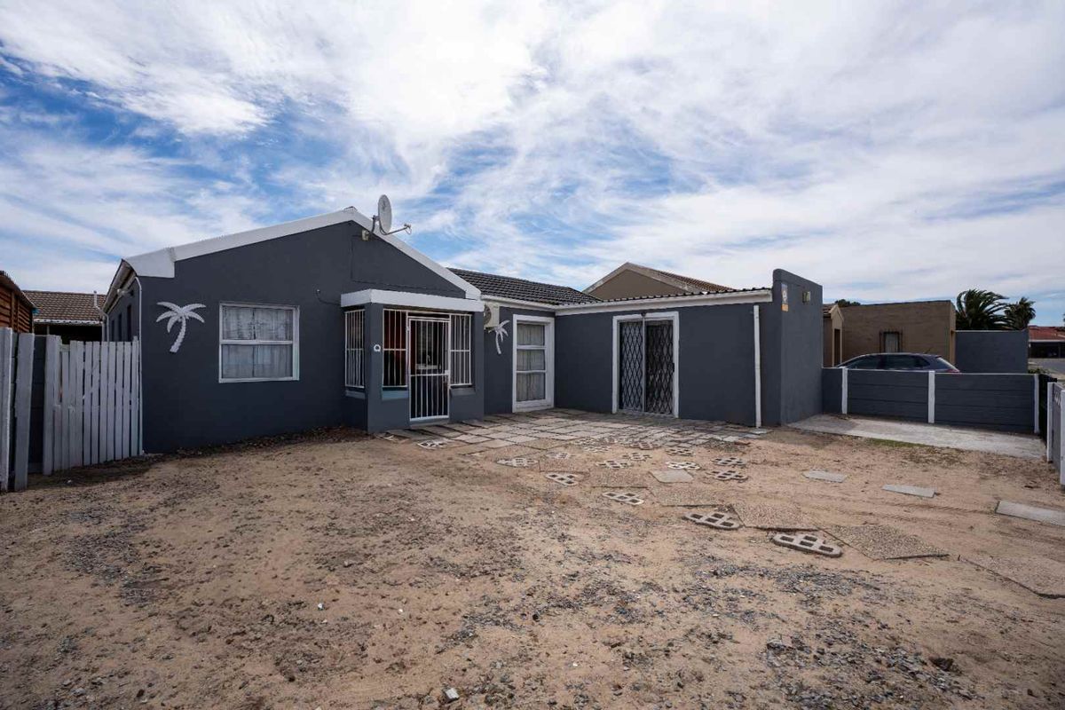 Rear exterior view of the property featuring a paved patio area, security gates, and a large unlandscaped yard space.