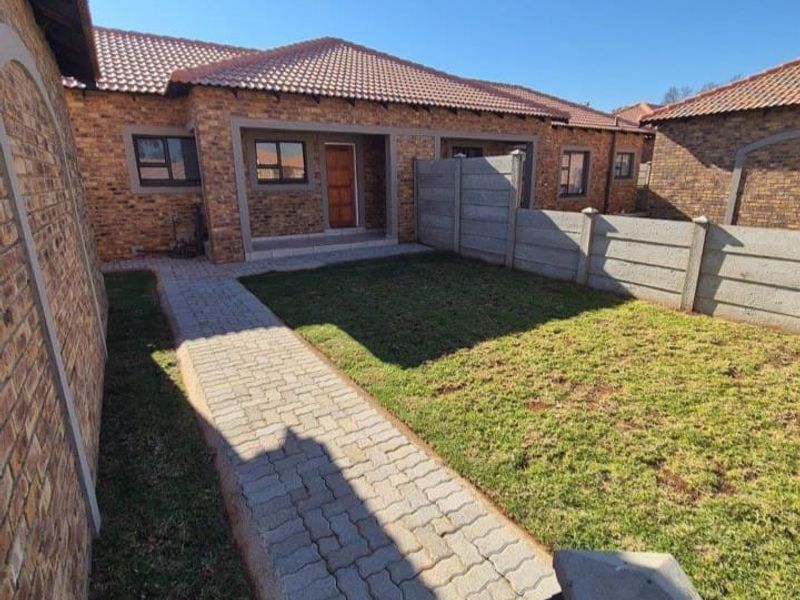 A rear view of a townhouse featuring a face brick exterior, tiled roof, paved walkway, and a private garden enclosed by precast concrete walls.