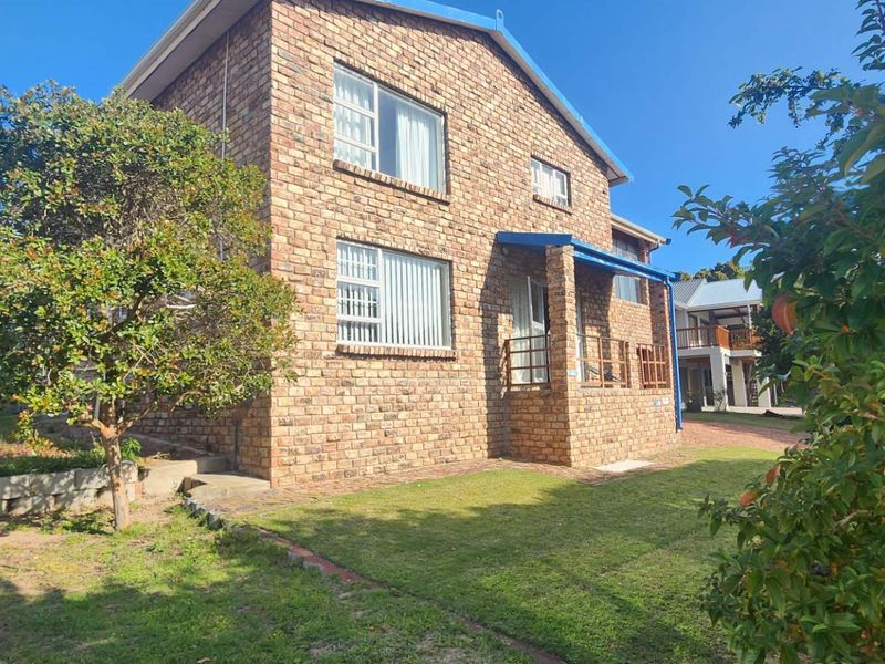 A two-story face-brick house featuring a covered entrance porch, aluminium window frames, and a well-maintained garden with a retaining wall.