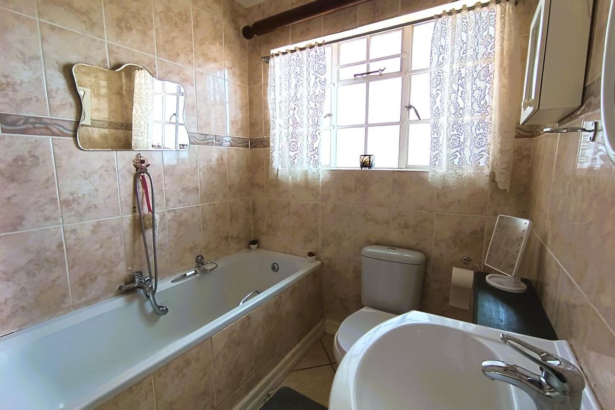 A functional bathroom featuring a built-in bathtub, pedestal sink, and toilet with neutral wall tiling and a window for natural light.