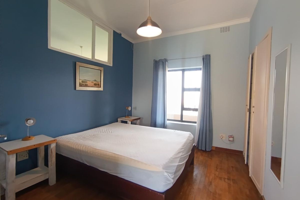 A bedroom featuring wooden flooring, a built-in cupboard, and a high-level transom window providing natural light.