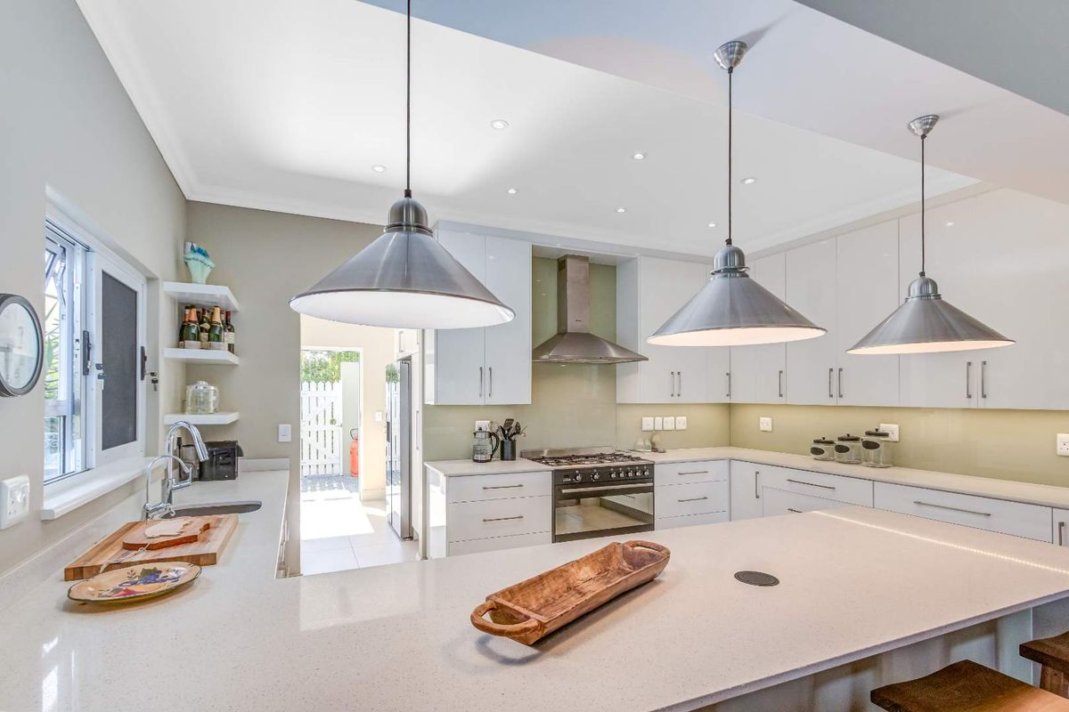Modern kitchen featuring white cabinetry, stone countertops, a central island, stainless steel gas stove, and an integrated extractor fan with recessed lighting.