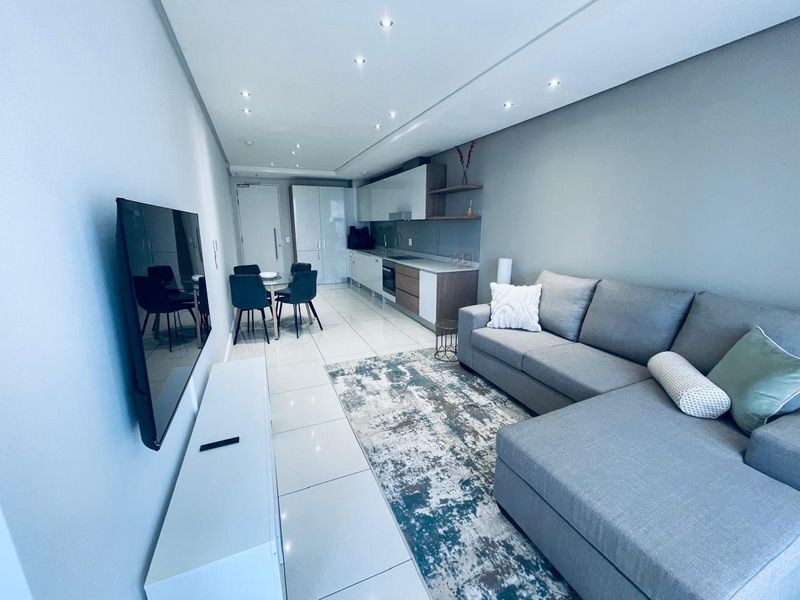 Modern open-plan living area featuring sleek kitchen cabinetry, integrated appliances, polished tiled flooring, and recessed downlighting in a contemporary apartment setting.