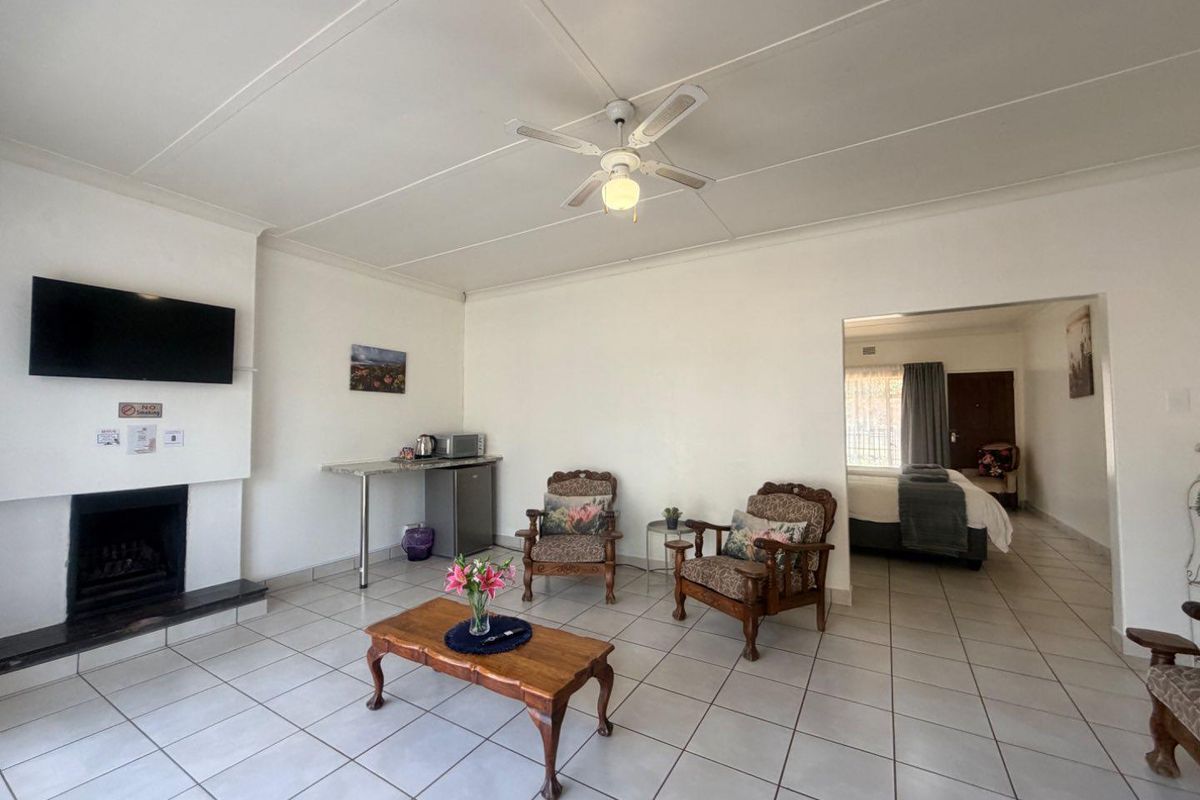 Spacious living area featuring a fireplace, ceiling fan, and neutral tiled flooring, with an open transition to the adjacent bedroom.