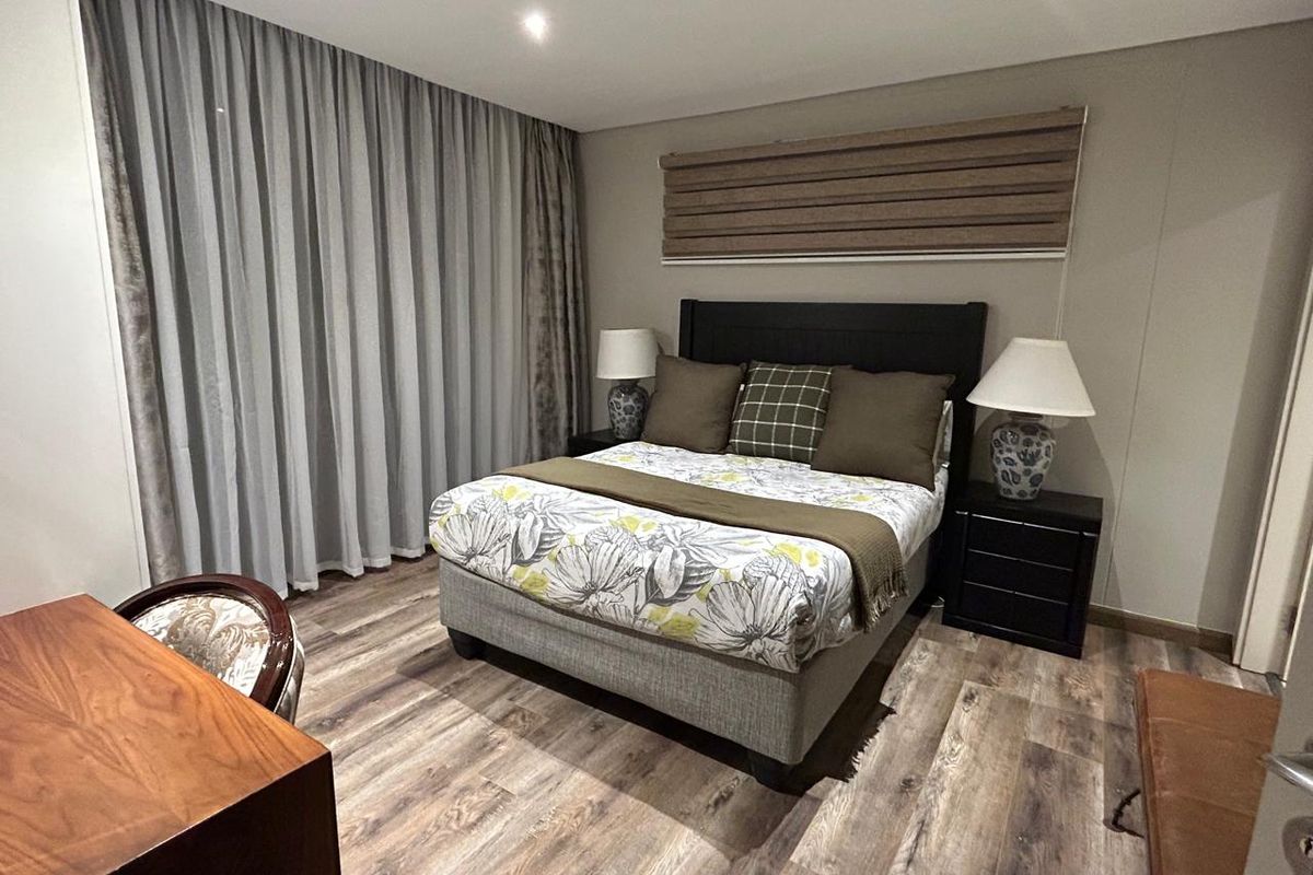 A well-maintained bedroom featuring modern laminate flooring, recessed ceiling lighting, and neutral wall finishes with integrated window treatments.