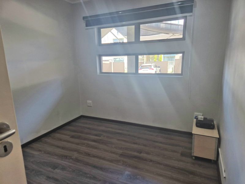 A clean, empty bedroom featuring modern dark laminate flooring and horizontal windows with a fitted roller blind.
