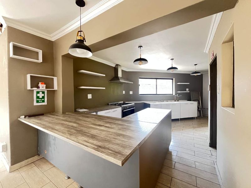 A spacious, open-plan kitchen featuring a large island, modern cabinetry, gas stove, extractor fan, and tiled flooring, offering a functional layout for cooking and entertaining.