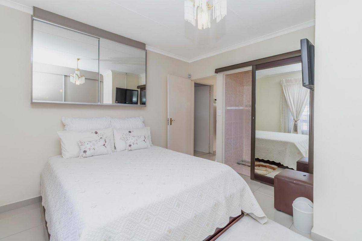 A well-maintained bedroom featuring built-in cupboards with mirrored sliding doors, neutral wall finishes, and tiled flooring.