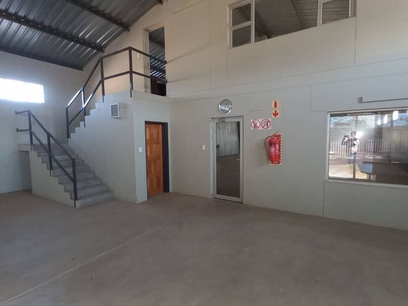 Spacious industrial utility area featuring concrete flooring, a mezzanine level with metal staircase, and integrated office partition with glass window.