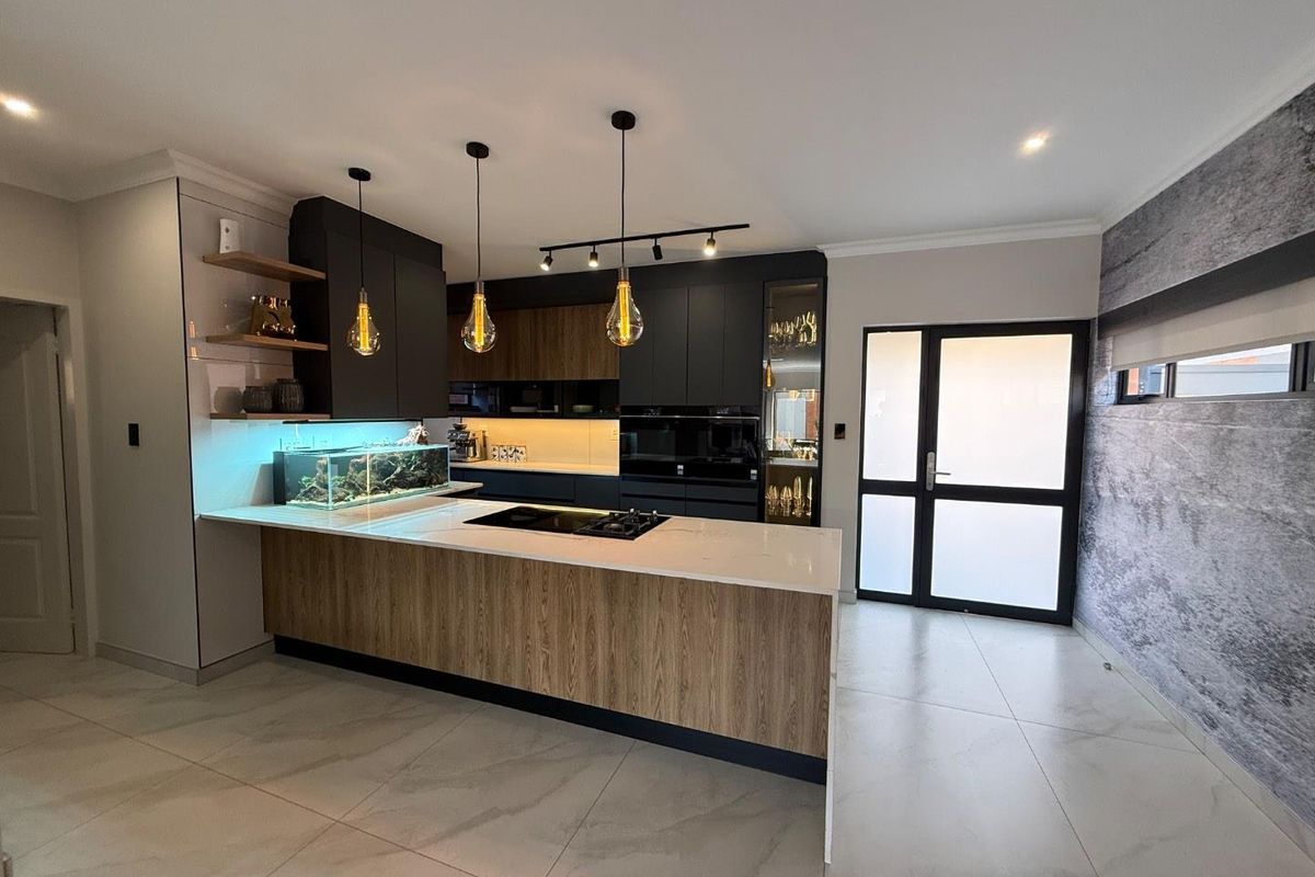 Modern open-plan kitchen featuring a large island with integrated cooktop, sleek dark cabinetry, stone countertops, and contemporary pendant lighting.