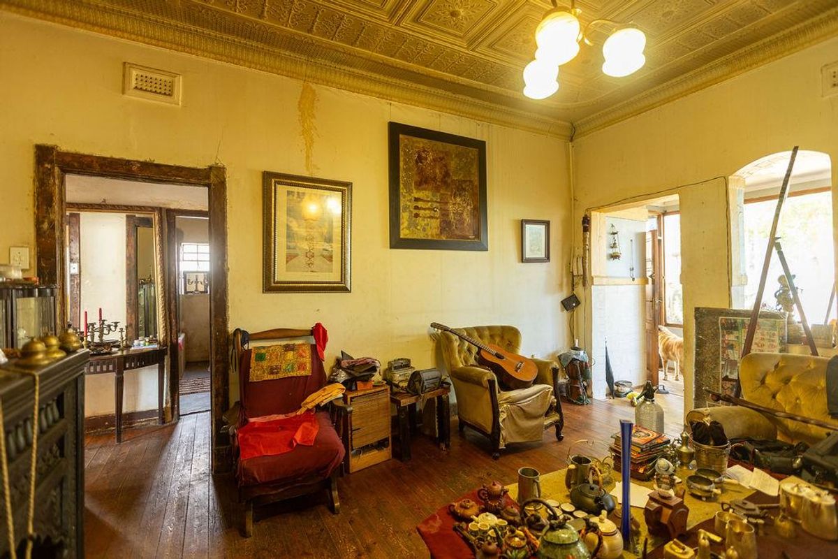 A living room featuring original pressed metal ceilings, timber flooring, and multiple doorways leading to adjacent rooms, showing signs of significant wear and aging.