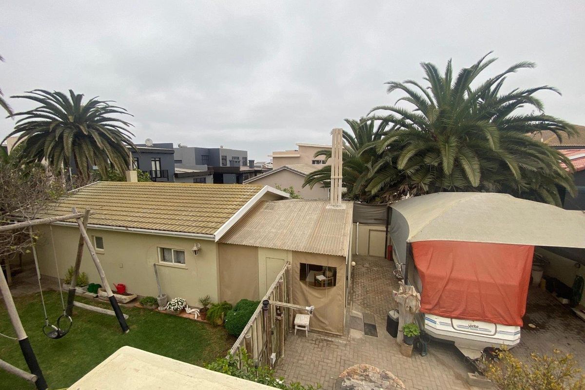 Elevated view of a rear garden area featuring a lawn, paved courtyard, and a covered outdoor structure with a chimney.