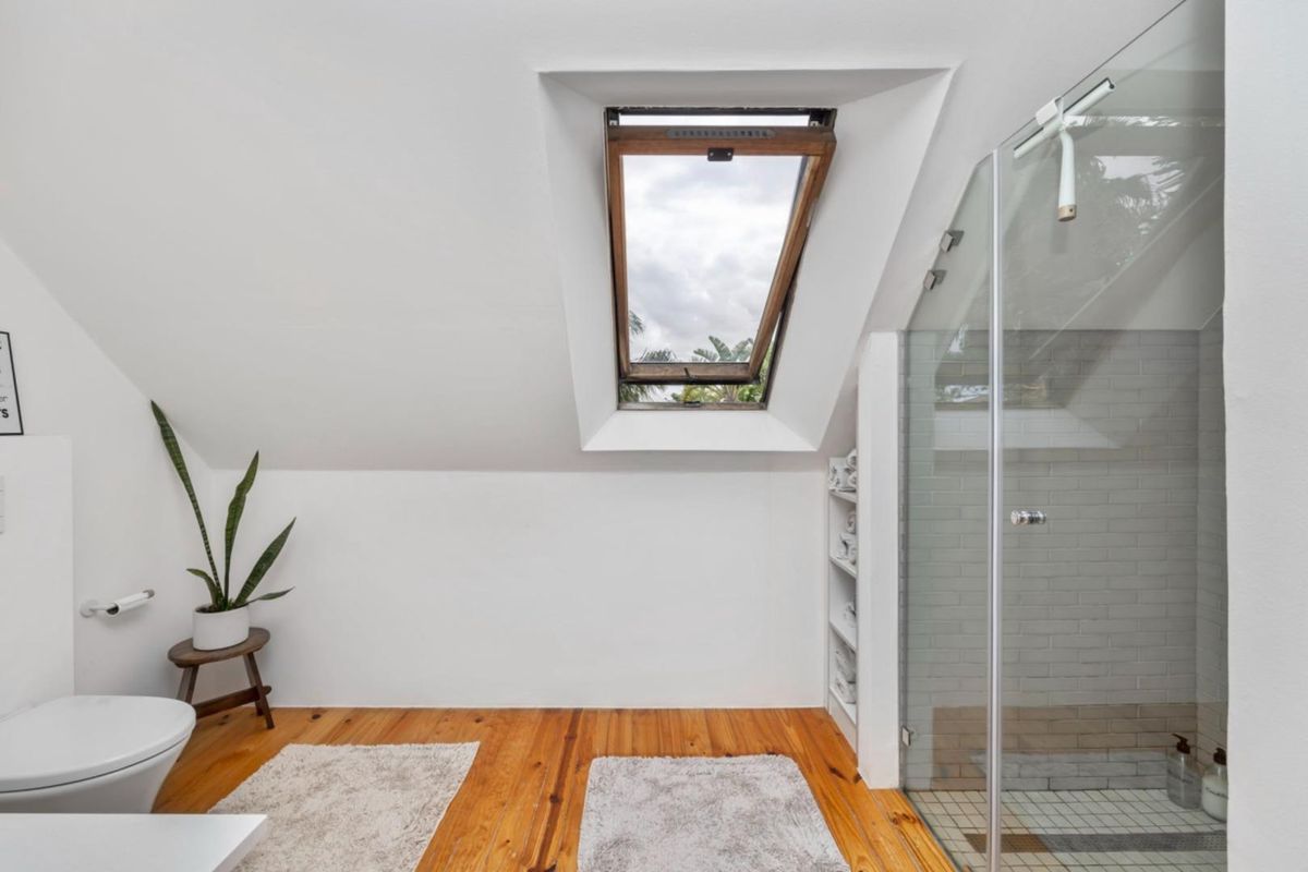 A bright attic bathroom featuring a glass-enclosed shower, timber flooring, and a skylight window providing natural light.