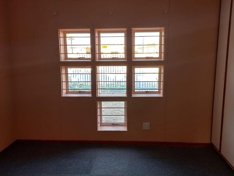 An empty bedroom featuring carpet flooring, built-in wardrobe storage, and a unique multi-pane window configuration with security bars.