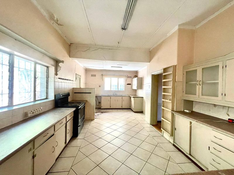 Spacious kitchen featuring original built-in cabinetry, tiled flooring, and a double sink, requiring significant renovation and cosmetic updates to restore its functionality.