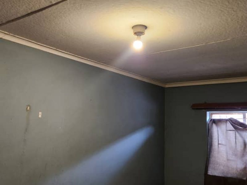An empty bedroom featuring blue painted walls, a textured ceiling with visible cracks, and a window fitted with security bars.