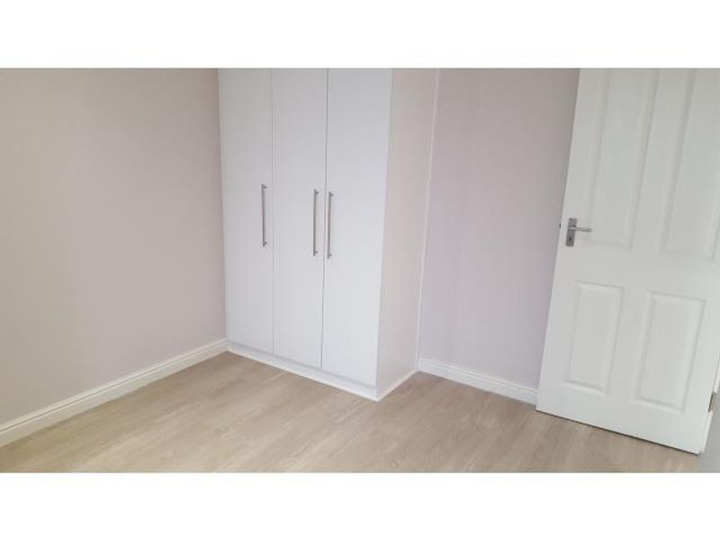 A clean, empty bedroom featuring light-toned laminate flooring, neutral walls, and a modern white built-in wardrobe.