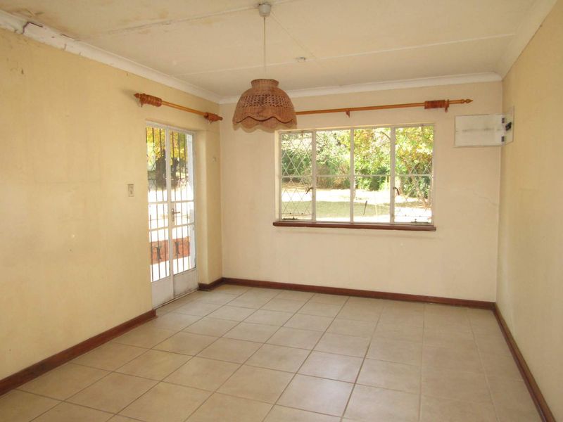 An empty living room featuring tiled floors, a security gate, and steel windows, requiring cosmetic updates to the walls and ceiling.
