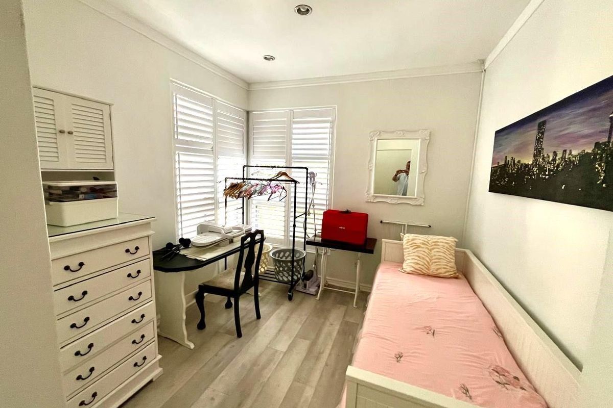 A well-lit bedroom featuring light-toned wood-look flooring, white plantation shutters, and recessed ceiling lighting.