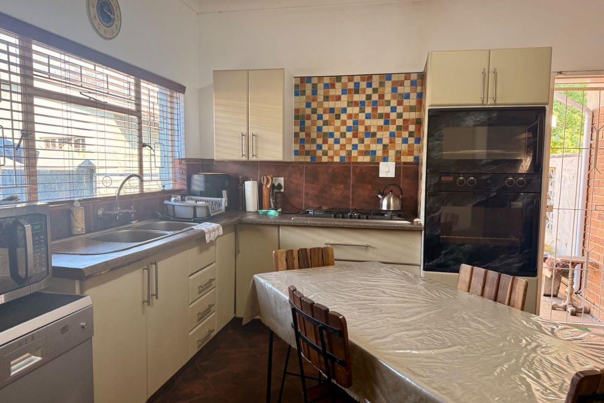 Functional kitchen featuring built-in cabinetry, integrated oven, gas hob, and double sink with tiled splashback and direct access to the exterior.