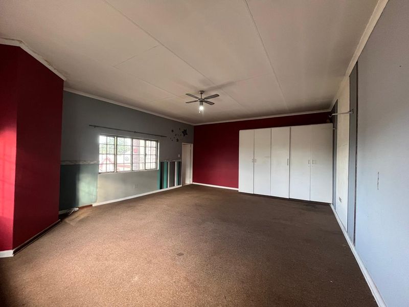 Spacious bedroom featuring built-in cupboards, a ceiling fan, and carpeted flooring. The room is vacant and ready for renovation or restyling.