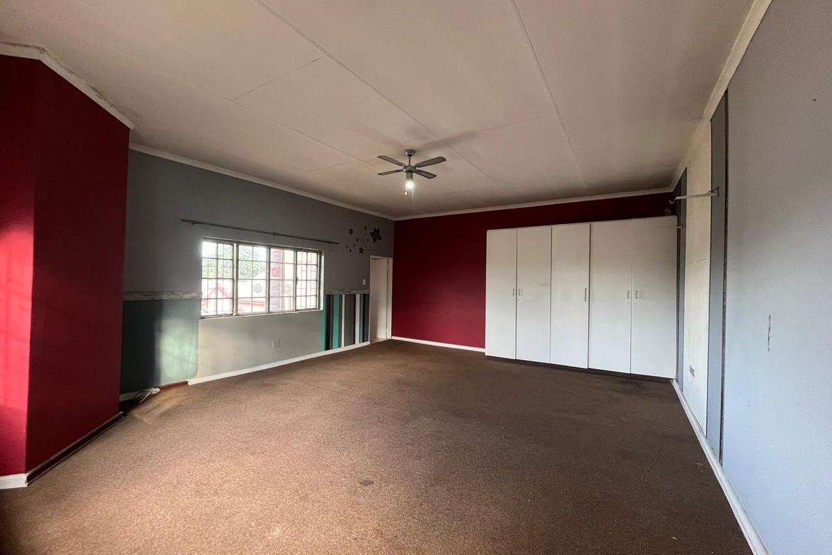 Spacious bedroom featuring built-in cupboards, a ceiling fan, and carpeted flooring. The room is vacant and ready for renovation or restyling.