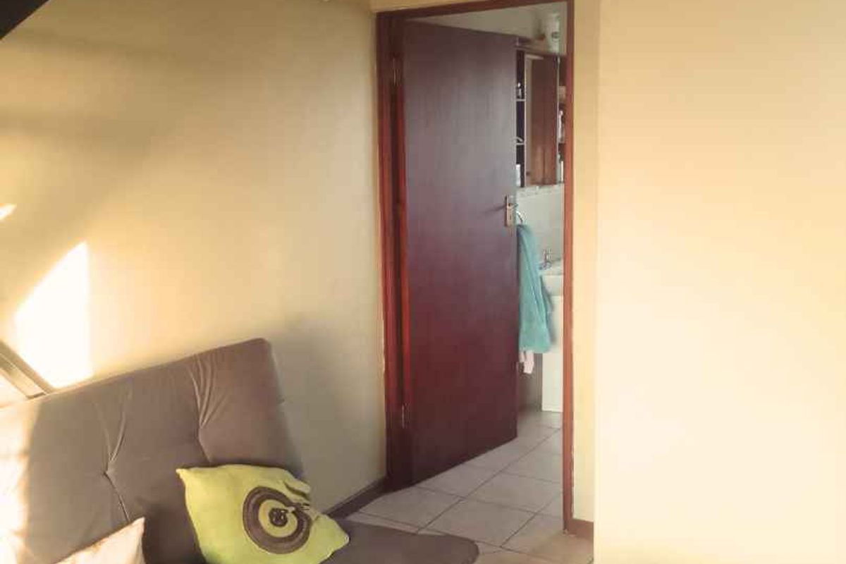 A view of a living area with tiled flooring, leading through a doorway into an adjacent bathroom space.