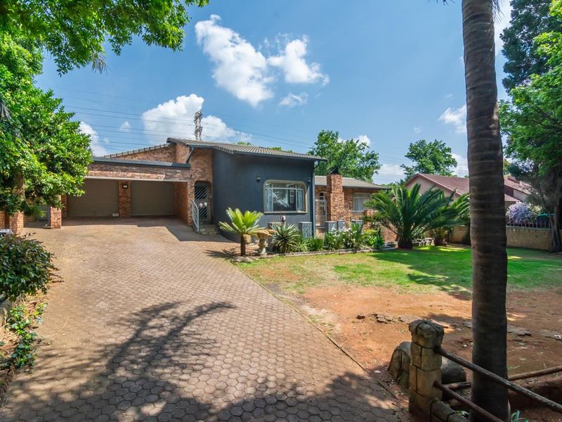 Front view of a brick house featuring a double garage, paved driveway, and established garden area.