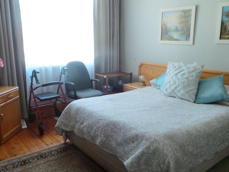 A bedroom featuring timber flooring and large windows with curtains, providing a functional and comfortable living space.