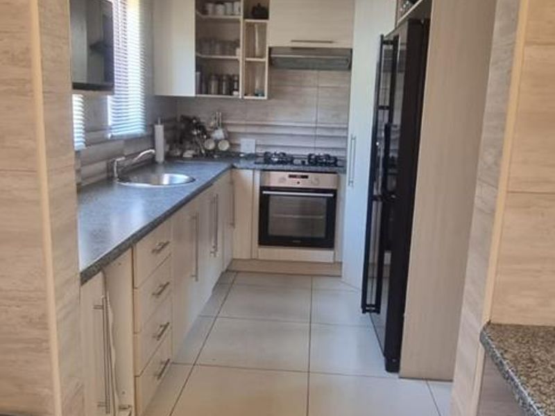 A functional galley-style kitchen featuring light-toned cabinetry, granite countertops, built-in oven, gas hob, and tiled finishes throughout.