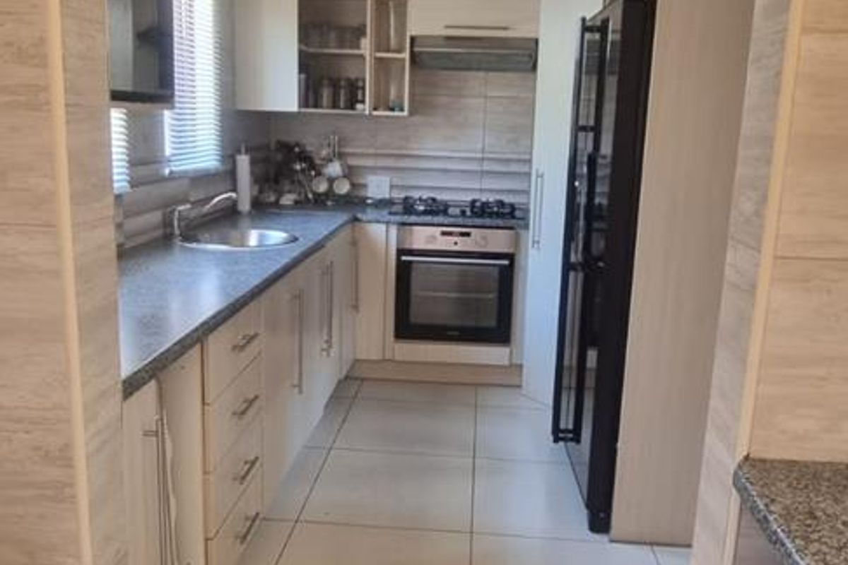 A functional galley-style kitchen featuring light-toned cabinetry, granite countertops, built-in oven, gas hob, and tiled finishes throughout.